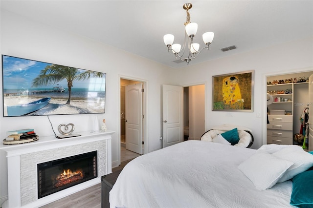 bedroom featuring a fireplace, wood-type flooring, a walk in closet, a notable chandelier, and a closet