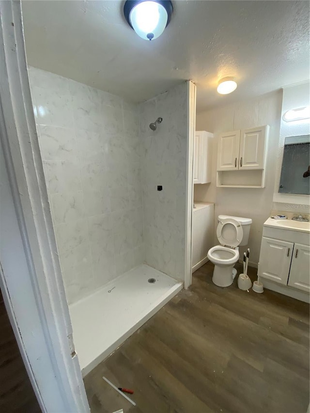 bathroom featuring toilet, tiled shower, wood-type flooring, and vanity