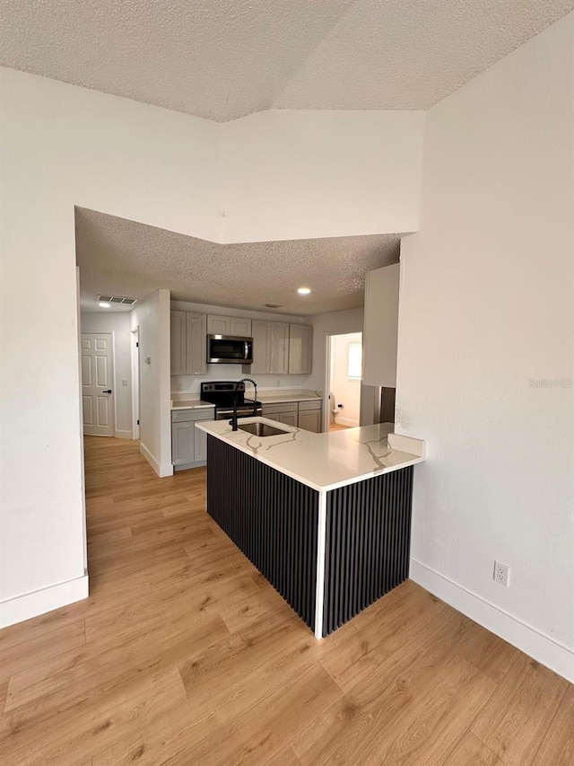 kitchen with gray cabinets, stainless steel appliances, light hardwood / wood-style floors, a textured ceiling, and kitchen peninsula