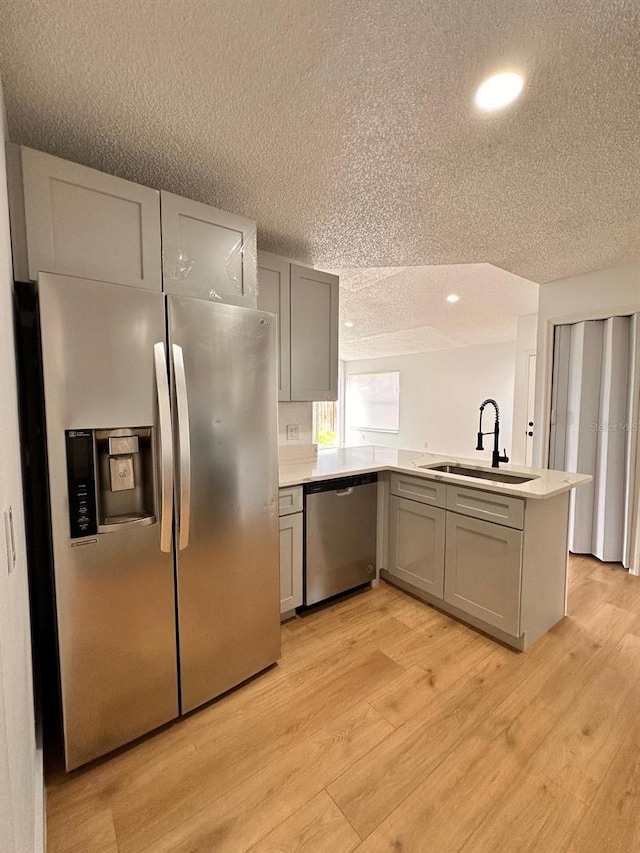 kitchen featuring stainless steel appliances, sink, light hardwood / wood-style floors, and kitchen peninsula