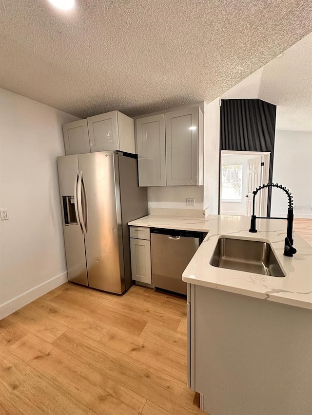 kitchen with gray cabinets, sink, light stone counters, stainless steel appliances, and light hardwood / wood-style flooring