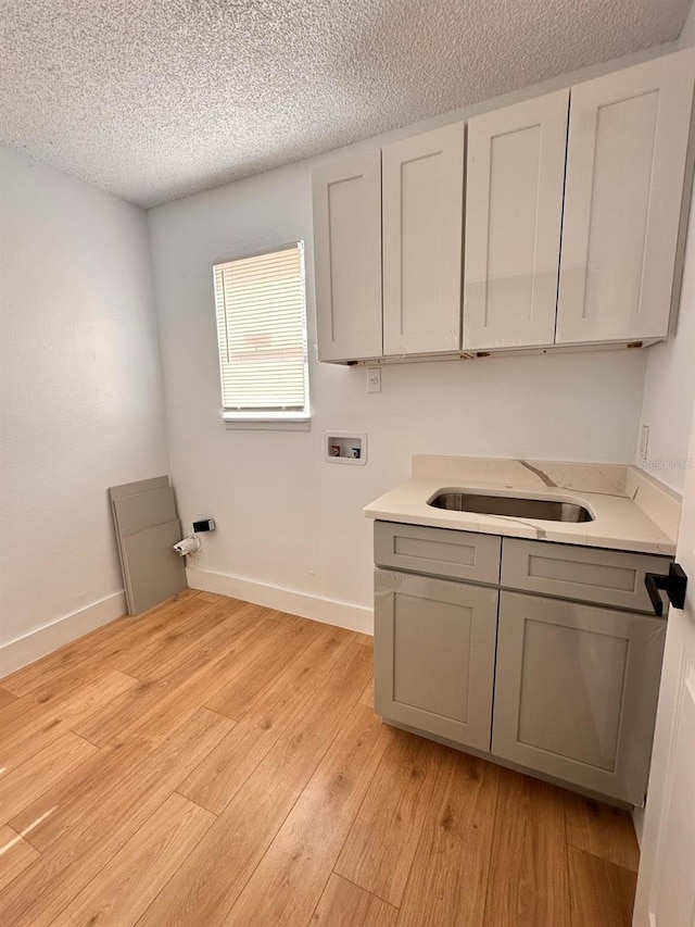 laundry room with sink, cabinets, a textured ceiling, light wood-type flooring, and hookup for a washing machine