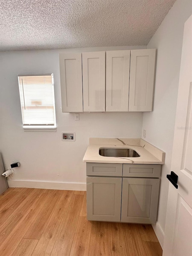 clothes washing area featuring washer hookup, sink, a textured ceiling, and light wood-type flooring