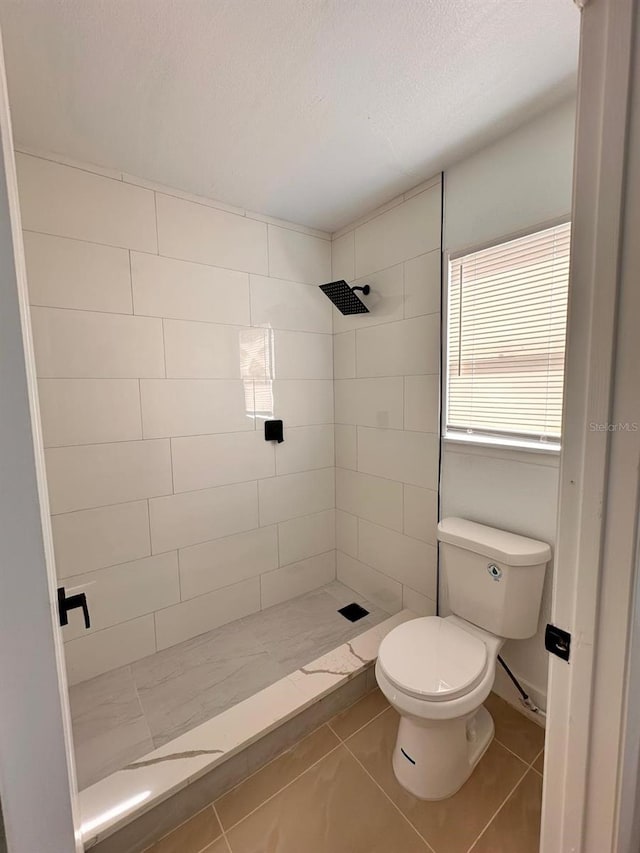 bathroom featuring tile patterned floors, toilet, a textured ceiling, and a tile shower