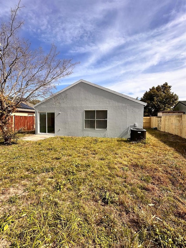 back of house with central AC unit and a lawn