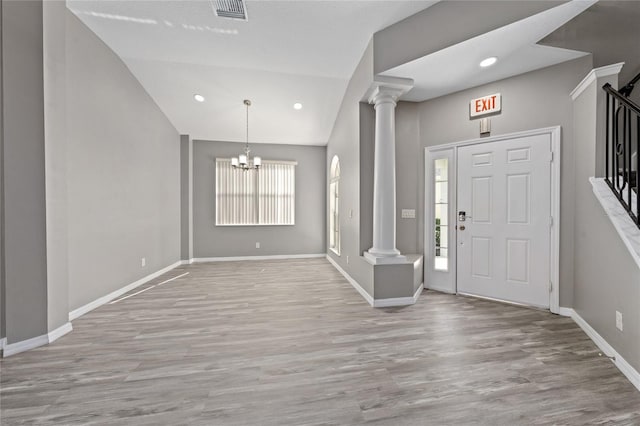 foyer entrance with a notable chandelier, vaulted ceiling, decorative columns, and light hardwood / wood-style floors