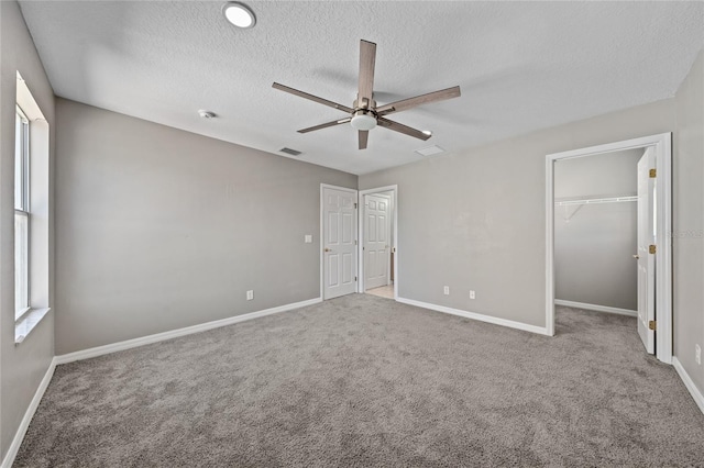 unfurnished bedroom featuring a walk in closet, a textured ceiling, carpet flooring, a closet, and ceiling fan