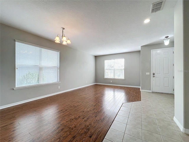 unfurnished room with light wood-type flooring, a textured ceiling, and an inviting chandelier