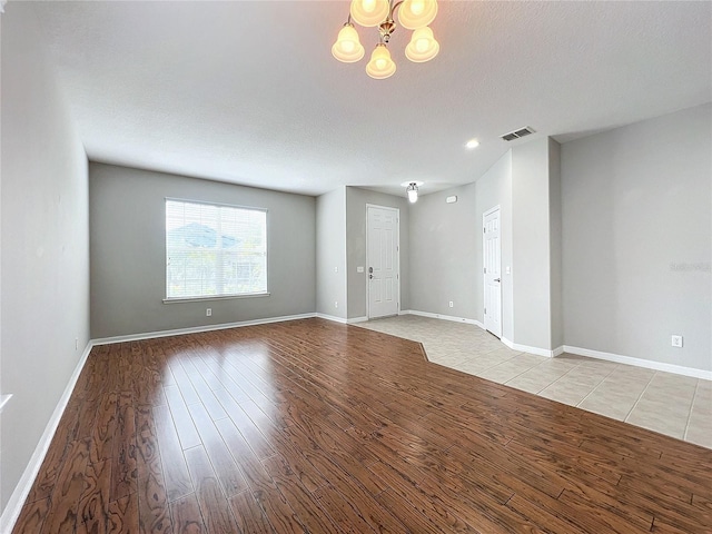 empty room featuring a textured ceiling, light hardwood / wood-style floors, and a chandelier