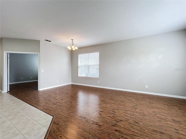 unfurnished room featuring a notable chandelier, a textured ceiling, and light hardwood / wood-style flooring