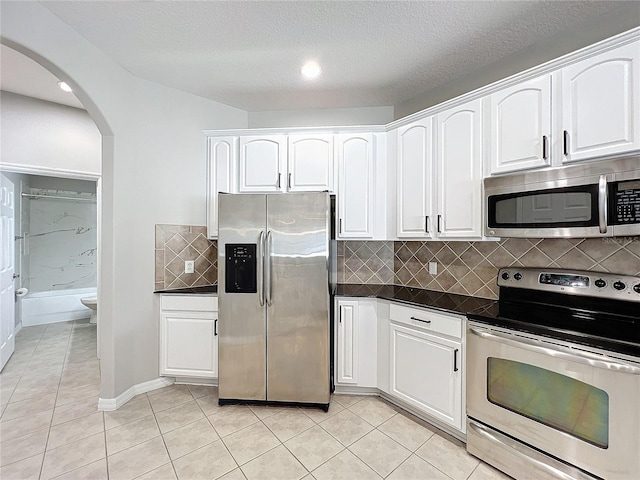 kitchen featuring light tile patterned floors, white cabinetry, stainless steel appliances, tasteful backsplash, and a textured ceiling