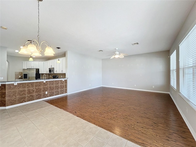 unfurnished living room with light hardwood / wood-style floors and ceiling fan with notable chandelier