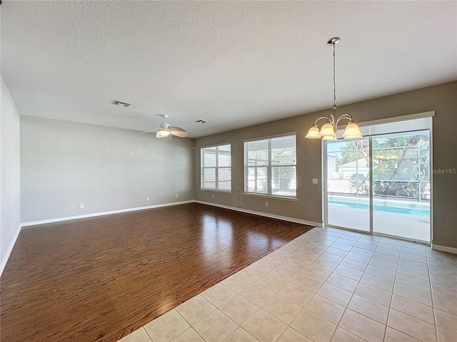 spare room featuring ceiling fan with notable chandelier, a textured ceiling, and light wood-type flooring