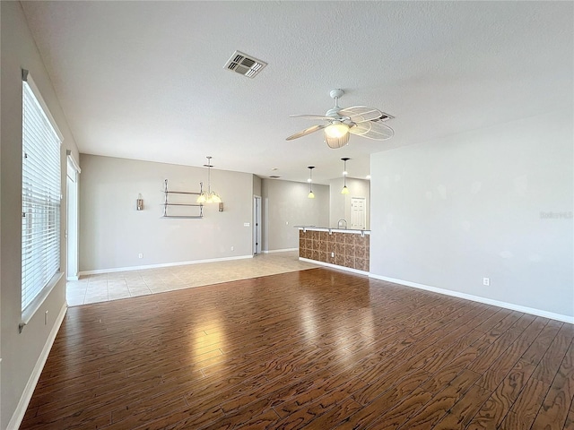 unfurnished living room with sink, ceiling fan with notable chandelier, a textured ceiling, and light wood-type flooring