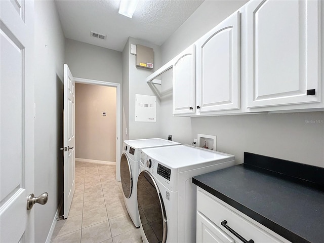 clothes washing area with washer and dryer, light tile patterned floors, cabinets, and a textured ceiling