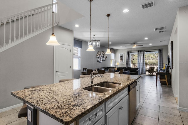 kitchen with pendant lighting, sink, dishwasher, light stone countertops, and a center island with sink