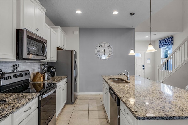 kitchen with sink, appliances with stainless steel finishes, a kitchen island with sink, white cabinetry, and hanging light fixtures