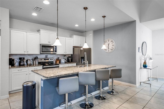 kitchen with pendant lighting, an island with sink, white cabinets, and appliances with stainless steel finishes