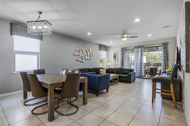 tiled dining space with ceiling fan with notable chandelier and a textured ceiling