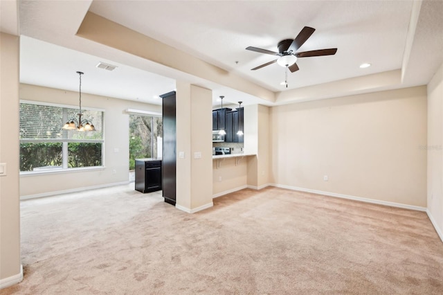 unfurnished living room with ceiling fan with notable chandelier, a raised ceiling, and carpet flooring