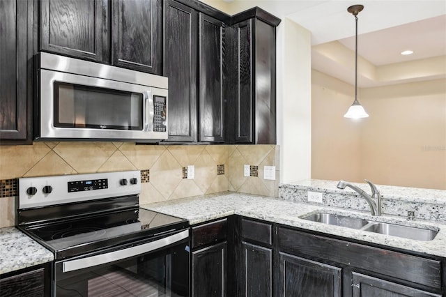 kitchen with sink, backsplash, stainless steel appliances, light stone countertops, and decorative light fixtures