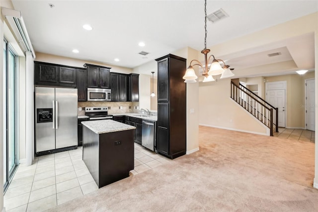 kitchen with a kitchen island, hanging light fixtures, light colored carpet, light stone counters, and stainless steel appliances