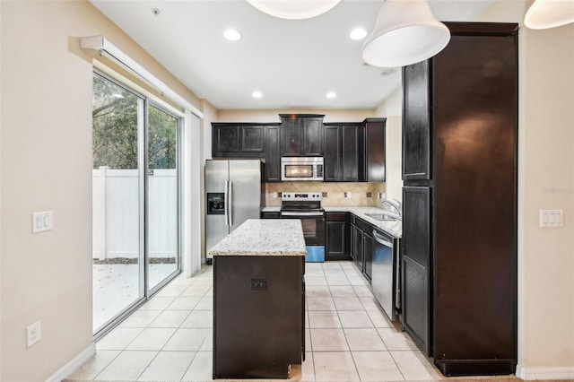 kitchen featuring sink, appliances with stainless steel finishes, a center island, light stone counters, and tasteful backsplash