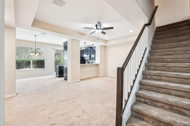 stairway featuring a raised ceiling, carpet floors, and ceiling fan with notable chandelier