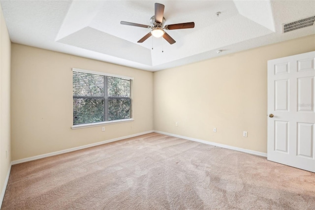 empty room with light carpet, a tray ceiling, a textured ceiling, and ceiling fan