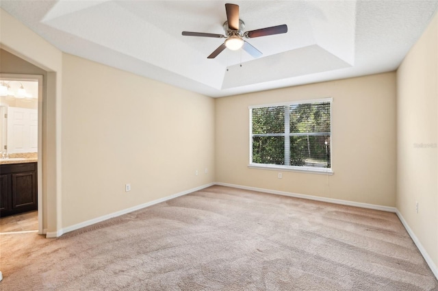 unfurnished room with light carpet, ceiling fan, and a tray ceiling