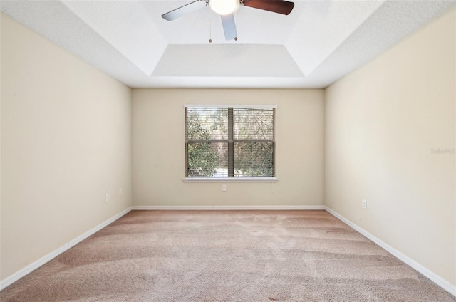 spare room with ceiling fan, light colored carpet, and a raised ceiling