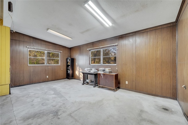 unfurnished office featuring lofted ceiling, plenty of natural light, a textured ceiling, and wood walls