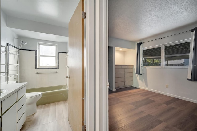 full bathroom featuring toilet, tiled shower / bath, wood-type flooring, a textured ceiling, and vanity