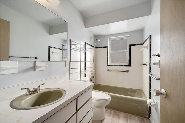 full bathroom with hardwood / wood-style flooring, tiled shower / bath, vanity, and toilet