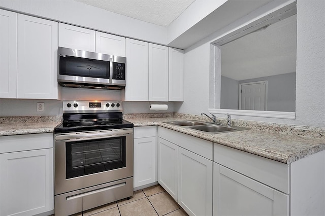 kitchen with light countertops, appliances with stainless steel finishes, light tile patterned flooring, a sink, and white cabinetry