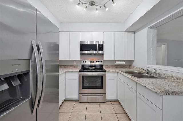 kitchen with appliances with stainless steel finishes, white cabinets, light tile patterned flooring, a sink, and a textured ceiling