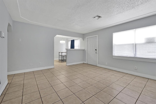 unfurnished room featuring arched walkways, visible vents, a textured ceiling, and baseboards