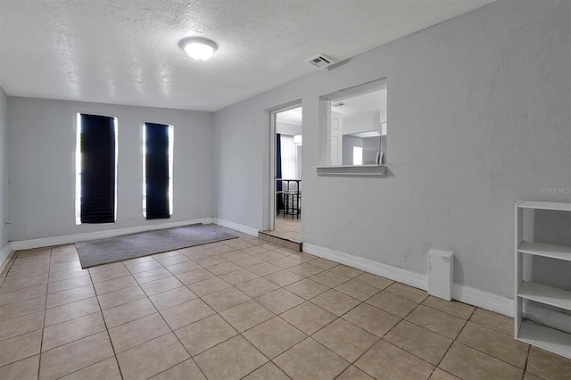 empty room featuring a textured ceiling, light tile patterned floors, visible vents, and baseboards