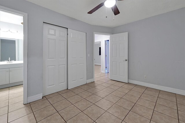 unfurnished bedroom with light tile patterned floors, a closet, baseboards, ceiling fan, and a sink