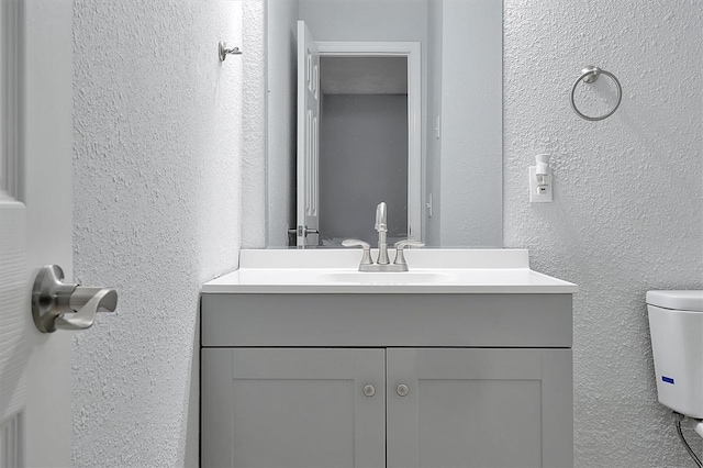 bathroom featuring a textured wall, vanity, and toilet