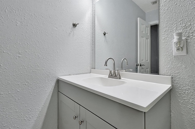 bathroom featuring visible vents, a textured wall, and vanity