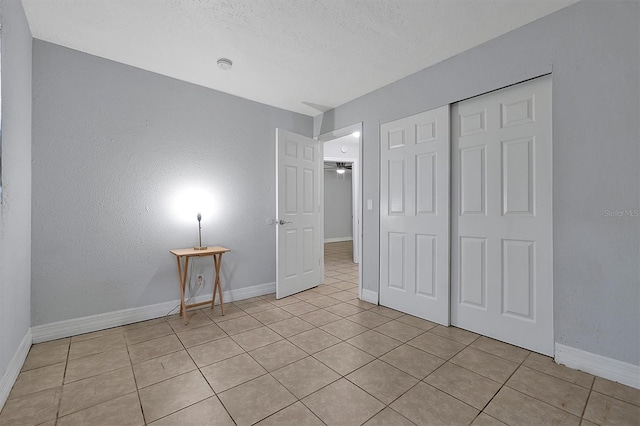 unfurnished bedroom with light tile patterned floors, a textured ceiling, baseboards, and a closet