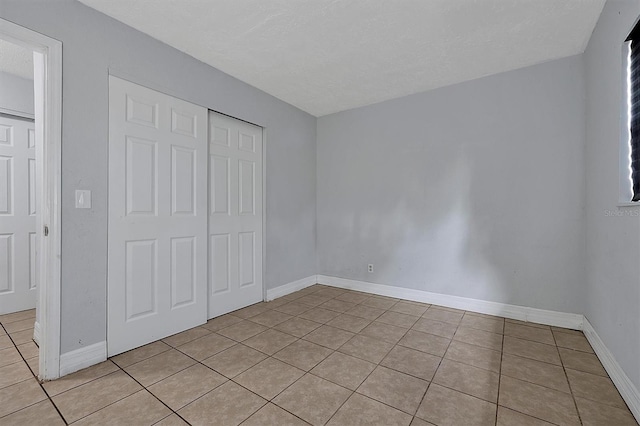 unfurnished bedroom featuring light tile patterned floors, a textured ceiling, baseboards, and a closet