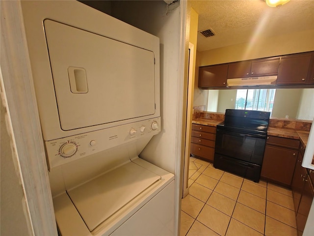 laundry area with light tile patterned flooring, stacked washer and clothes dryer, and a textured ceiling