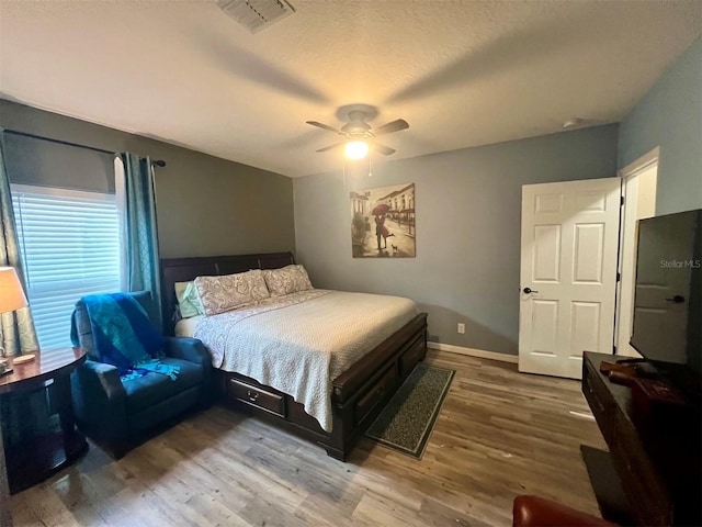 bedroom with a textured ceiling, wood-type flooring, and ceiling fan