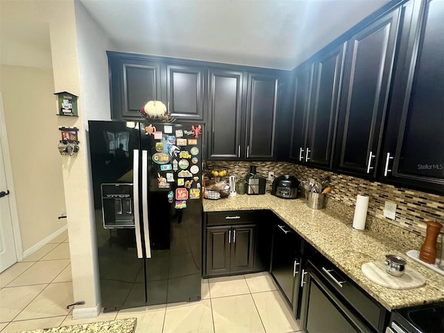 kitchen with light stone counters, black fridge with ice dispenser, decorative backsplash, and light tile patterned floors