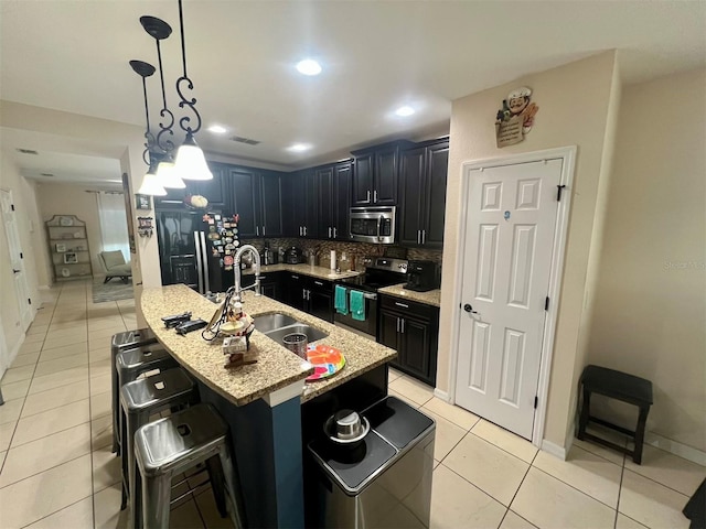 kitchen with a kitchen bar, sink, a center island with sink, light tile patterned floors, and appliances with stainless steel finishes