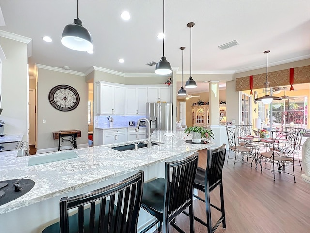 kitchen with white cabinetry, sink, a kitchen bar, hanging light fixtures, and stainless steel refrigerator with ice dispenser