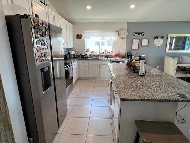 kitchen with appliances with stainless steel finishes, white cabinets, dark stone counters, a center island, and light tile patterned floors