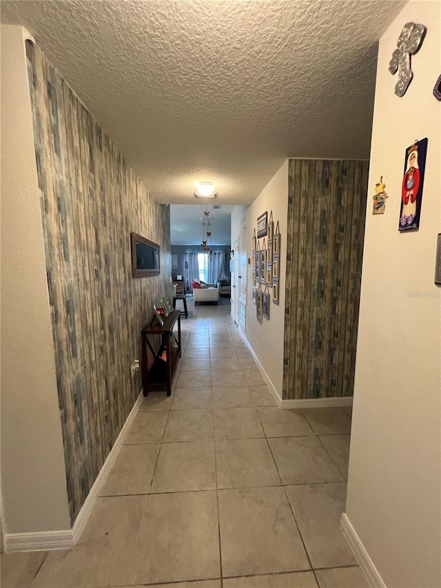 corridor featuring tile patterned floors, a textured ceiling, and wood walls